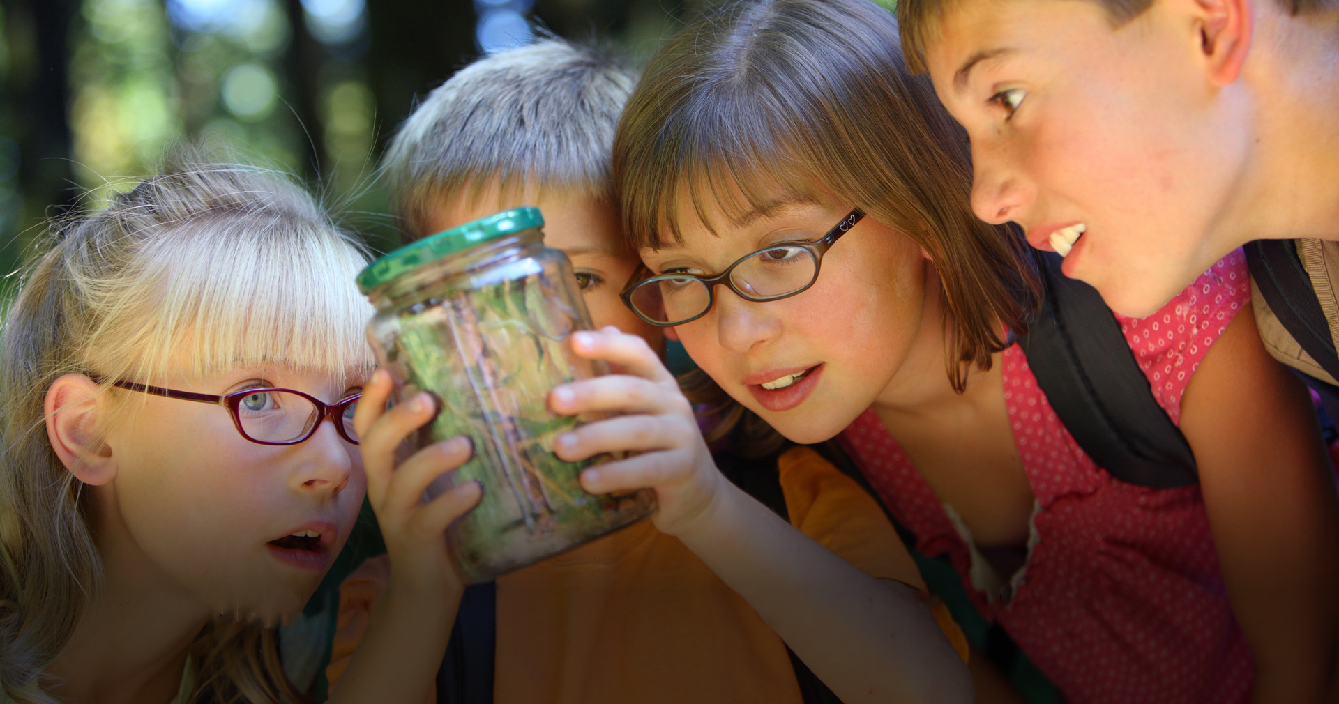 Children curiously examining a jar together outdoors